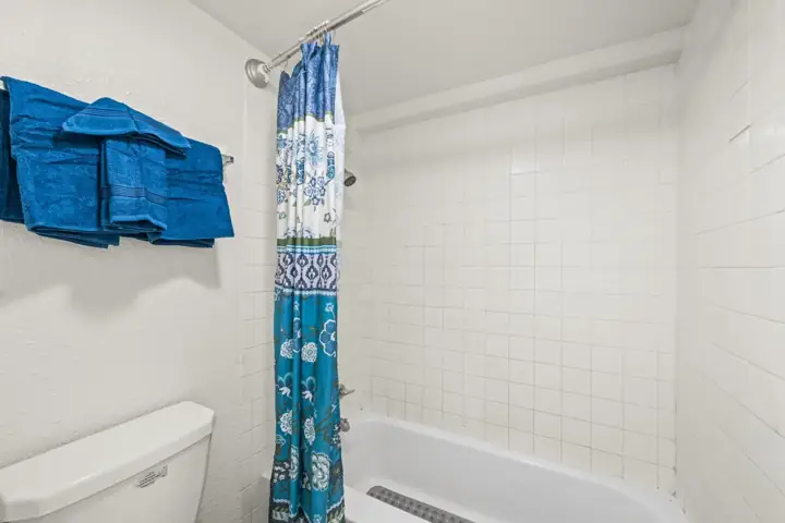 Bathroom shower area with a blue floral shower curtain, white tiled wall, and three blue towels on a wall-mounted towel rack