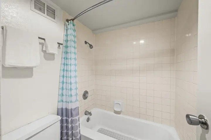 Bathroom shower area with beige tiled walls, a white bathtub, a blue and white polka dot shower curtain, a wall-mounted