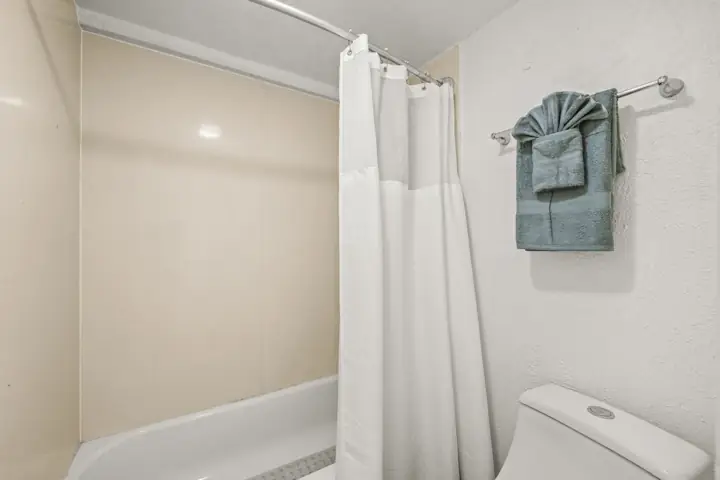 Bathroom with a shower and a toilet, beige and white walls, a white shower curtain, and gray towels hanging on a