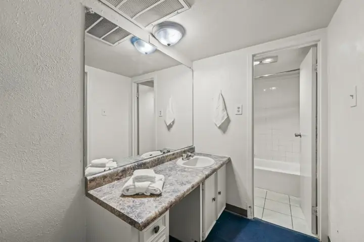Bathroom with white walls, a granite countertop with a sink, a large mirror, and a towel hanging on the wall. There is a