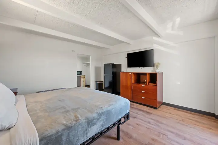 Bed, dresser, TV and full-size refrigerator in a renovated room