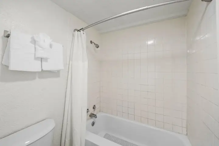 Empty bathroom with bathtub, shower head, curtain, towel rack with folded white towels, and beige tiled walls