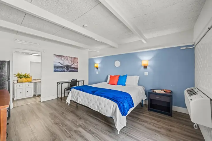 Hotel room with a bed, pillows, and a blue and white color scheme, including wall-mounted lamps and a small table with