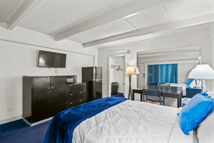 Hotel room with two beds, a dark wood dresser, a small refrigerator, a TV mounted on the wall, a nightstand, a lamp, a