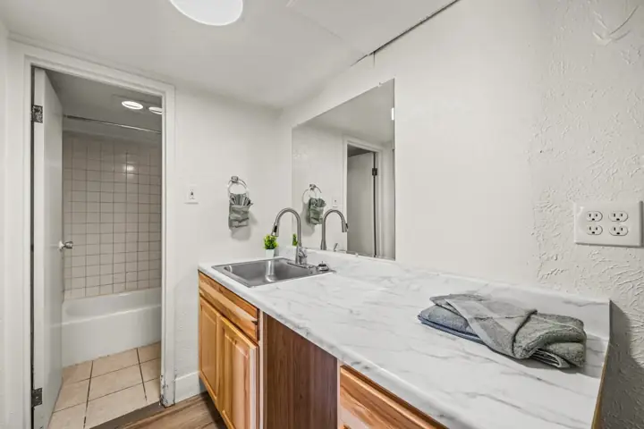 Kitchen with white marble countertop, wooden cabinets, a stainless steel sink, and a large mirror on the wall. Towels