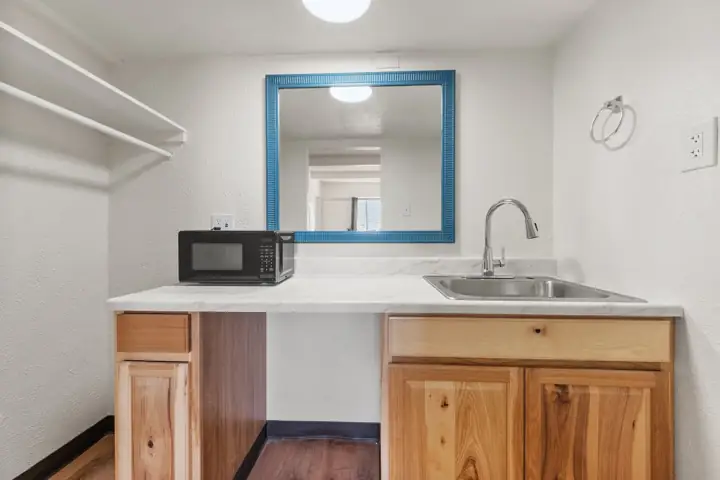 Kitchenette sink and wood cabinets below a blue-framed mirror
