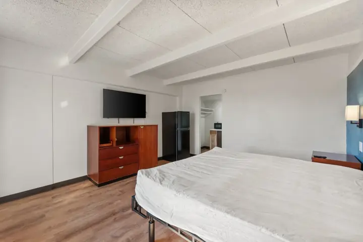 Renovated room with a dresser, wall-mounted TV and full-size refrigerator