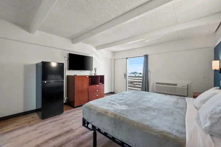 Room with a full-size black refrigerator, dresser, wall-mounted TV and balcony door