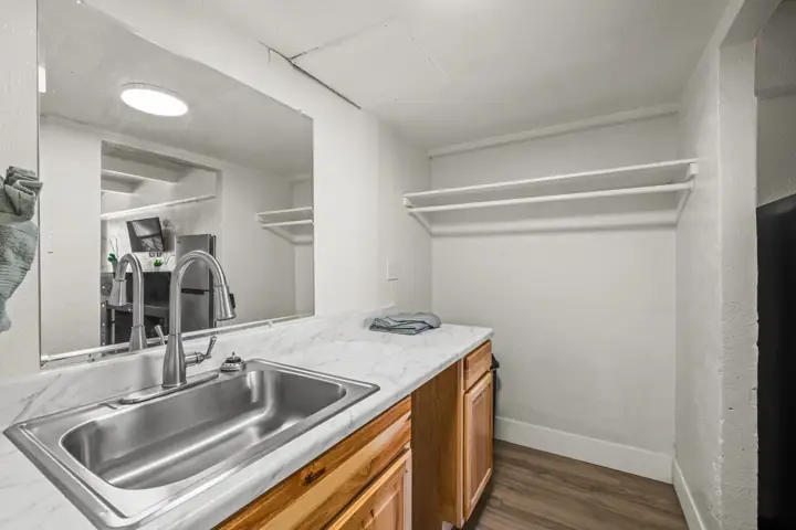 Small utility area with a stainless steel sink, wooden cabinets, a marble countertop, and white wall shelves