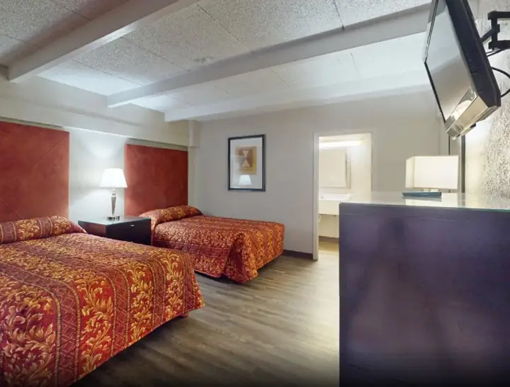 Two beds with red patterned bedspreads and a wall-mounted TV